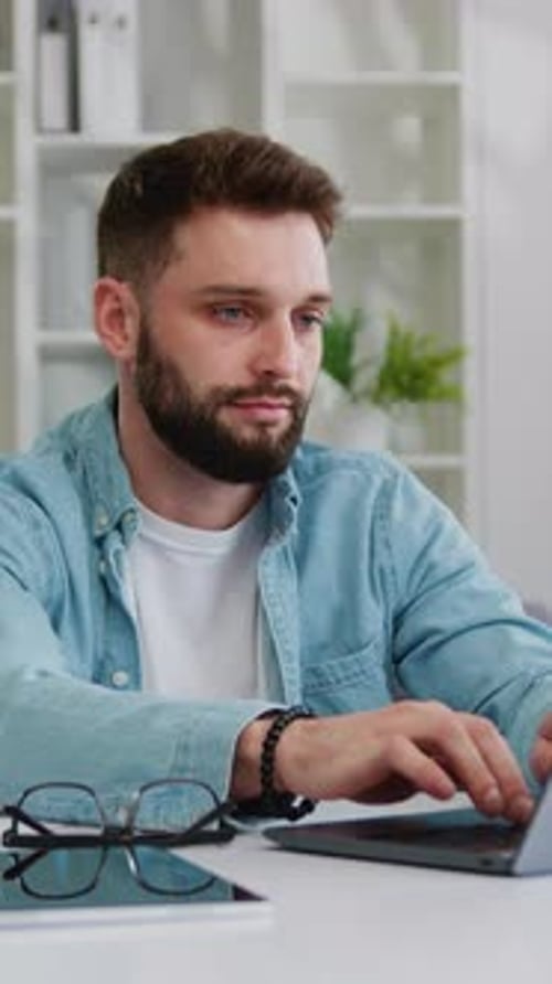 Ernsthafter junger bärtiger Geschäftsmann tippt auf einem Laptop, arbeitet online, schreibt E-Mails, während er sitzt