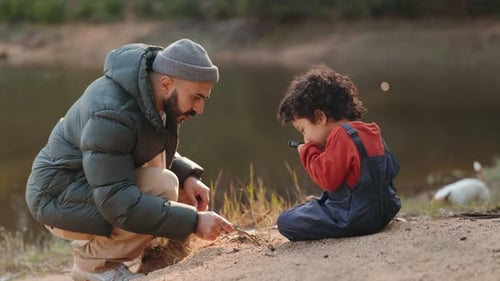 Père et fils explorant la nature au bord d'un lac avec une loupe