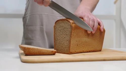 Person Slicing Loaf of Bread in Kitchen