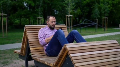 Young man enjoys music on cellphone relaxing in the park near New York City