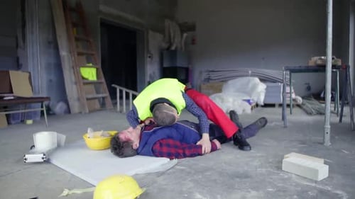 Man checks injured construction worker lying on floor