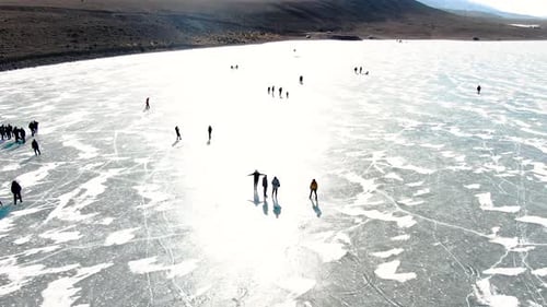 Aerial slow motion view of people ice skating on a frozen lake
