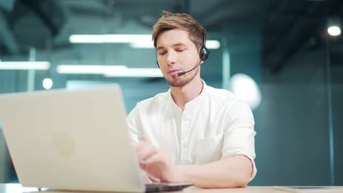 Smiling man call centre operator, customer support agent wears headset consults client online typing