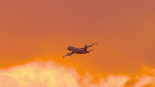 Airplane Flying through Dramatic Orange Sky at Sunset