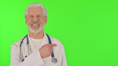Portrait of Pointing Senior Doctor Showing Copyspace on Green Background