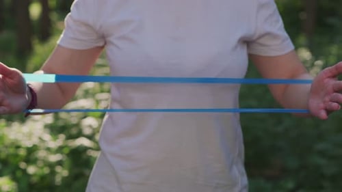 A Woman in a White Shirt and Headband Stretches Her Arms with a Resistance Band in a Forest Setting