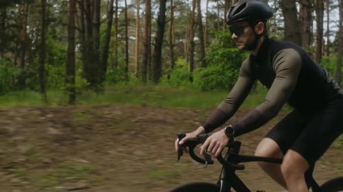 Mann im schwarzen Trainingsanzug fährt professionelles Fahrrad durch den Pinienwald