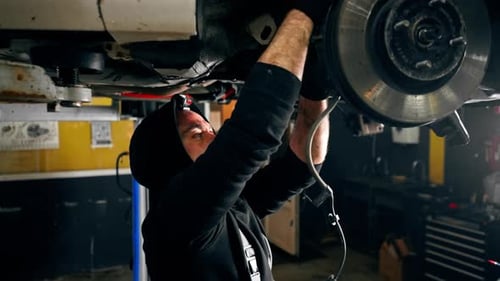 an Auto Mechanic at a Service Station Tightens the Bolts Under the Wheel with a Wrench