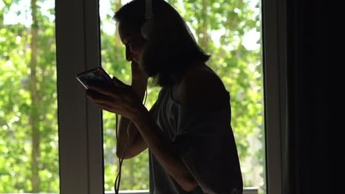 Woman listening to music and using smartphone indoors