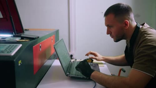 Technician Programming Laser Engraving Machine with Laptop