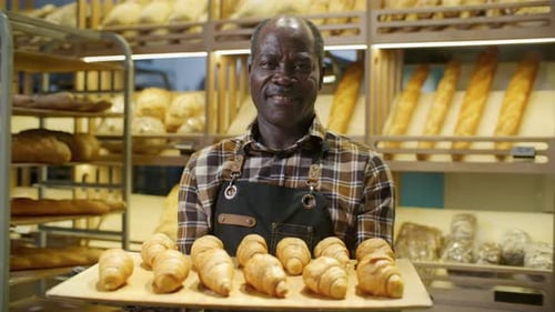Smiling Baker Holding Tray of Croissants in Bakery