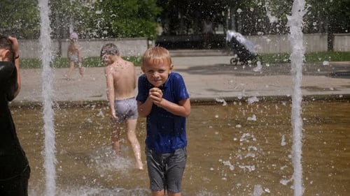 Two Cheerful Children Play in the Fountain in the Summer in the City Park