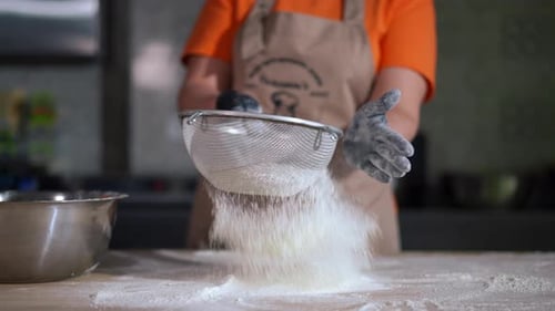 Person Sifting Flour onto a Wooden Table
