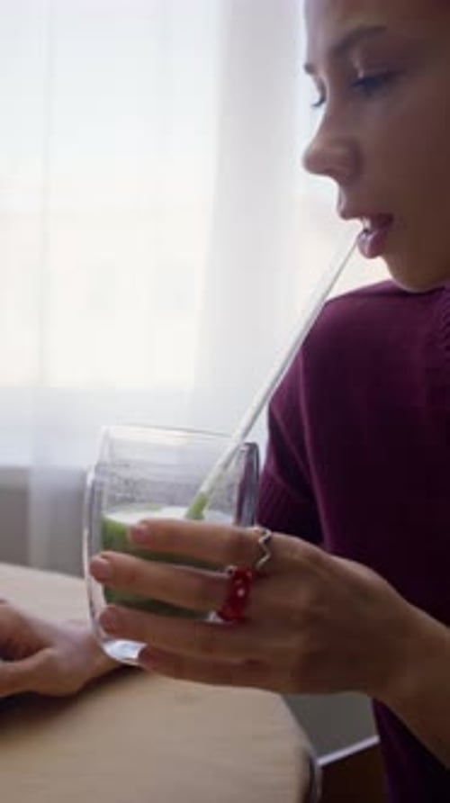 Young Woman Drinking Green Smoothie while Working on Laptop