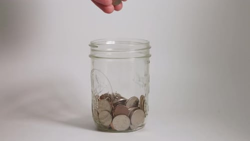 Hand Placing Coins in Glass Jar for Savings