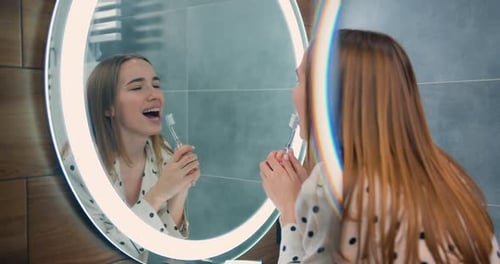 Happy Woman Brushing Teeth in Bathroom Mirror