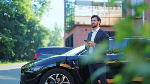 Mann lädt Elektrofahrzeug glücklich über die digitale Smartphone-Verbindung auf