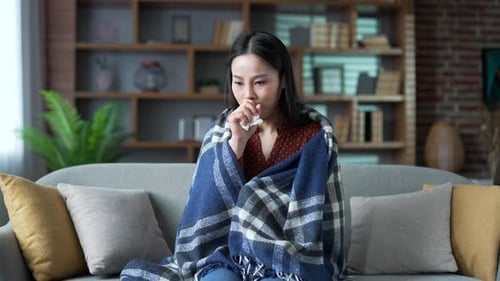 Malade d'un rhume, une jeune femme asiatique adulte tousse assise sur le canapé du salon à la maison