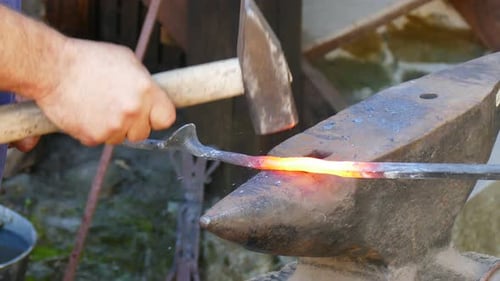 Blacksmith Forging Glowing Metal on Anvil with Hammer