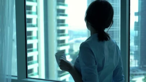Young businesswoman enjoys morning coffee and city view from her office window