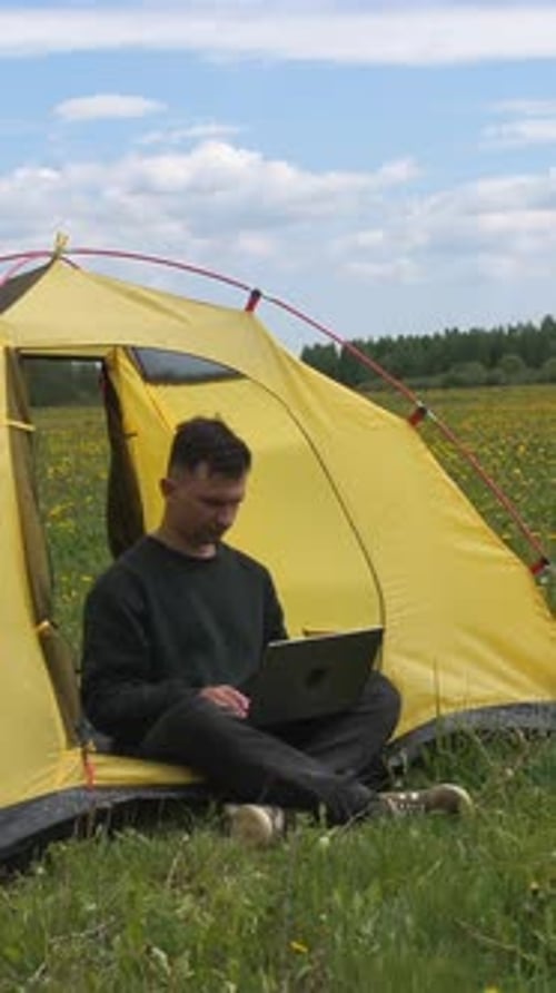 Vídeo vertical: Trabalhador freelancer em um laptop enquanto está sentado em uma barraca