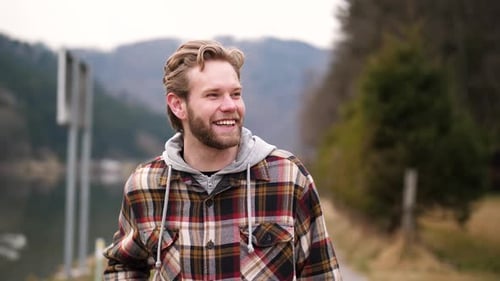 a hearty laugh of a young man walking along a path next to a river whitewashes this video in an autu