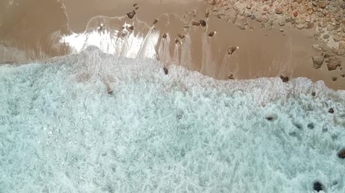 White water waves and beach with some rocks, top down drone shot