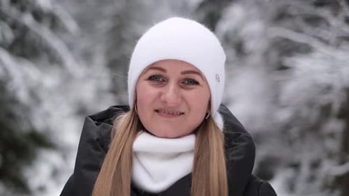 Close Up Portrait of Young Woman in Warm White Hat Looking at Camera Outdoors on Winter Forest