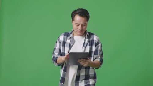 Asian Man Using Tablet While Walking On Green Screen In The Studio