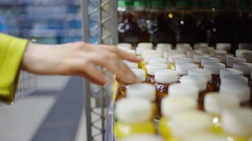 A Closeup View of a Shopper's Woman Hand Picking a Jar of Juice From a Supermarket Shelf with Rows