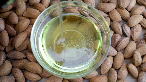 Almond Oil is poured into transparent bowl, view from above. Yellow Cold Pressed Almond Oil.