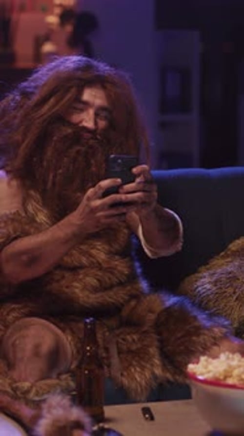Smiling Caveman Using Smartphone on Couch at Home