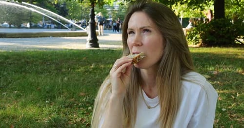 Woman Eats Bread in Urban Park by Fountain