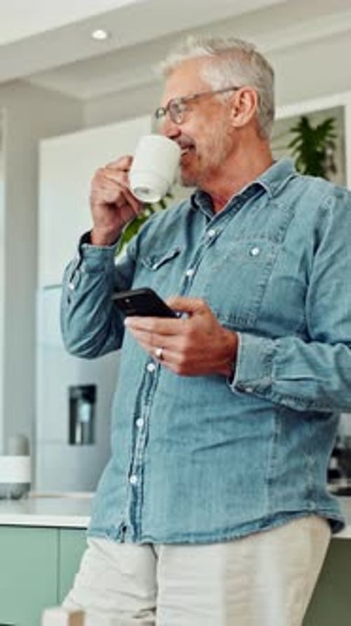 Senior Man Drinks Coffee While Using Smartphone Indoors