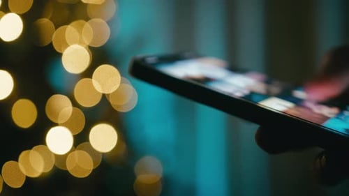 Hand Flips Through Photos on a Smartphone at Night in Front of a Christmas Tree