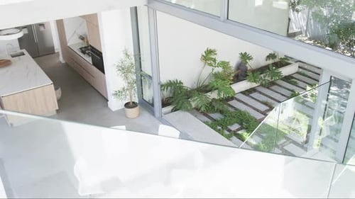 A modern kitchen with marble countertops overlooks a small garden with lush greenery