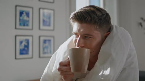 Man Wrapped in Blanket Drinks Morning Beverage