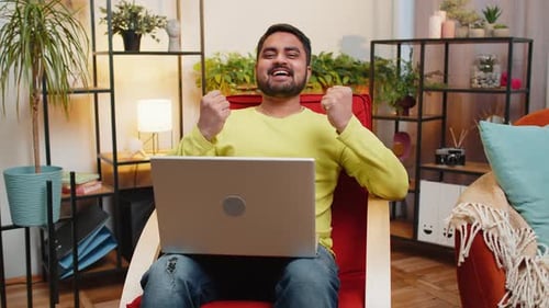 Man Celebrates Success Using Laptop at Home
