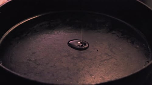 Vue rapprochée de la cuisine : de l'huile est versée dans une poêle en fonte sous un éclairage tamisé