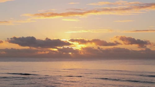 Golden Sunrise Over Ocean Horizon with Clouds Reflecting the Morning Light Serenely