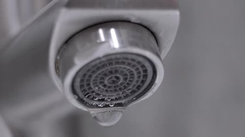 Water dripping from modern faucet forming drops