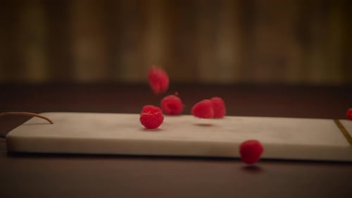 Fresh Raspberries Falling on a Marble Cutting Board