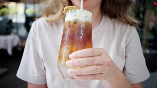 Close view of a woman holding and drinking a cold brew espresso shot drink with matcha foam and stra