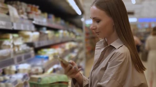 Young Woman in the Grocery Shop During Choosing and Buying Fresh Chicken Eggs She Scans the QR Code