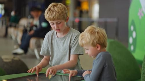 Young Boy With Older Brother Looking At Touchscreen In Airport