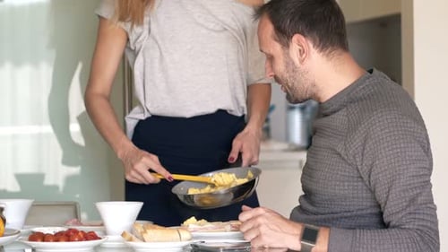 Woman Cooking Scrambled Eggs for Man at Breakfast