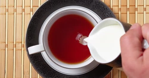 Adding Milk From a Jug to a Cup with Black Fragrant Tea Top Down View