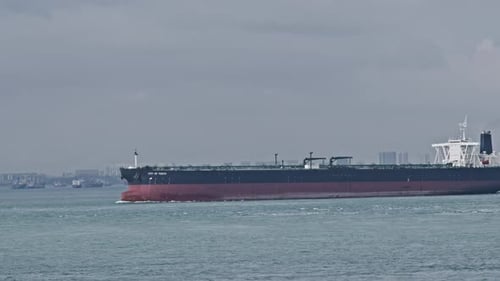 A large cargo ship sails across a calm sea with other vessels in the distance