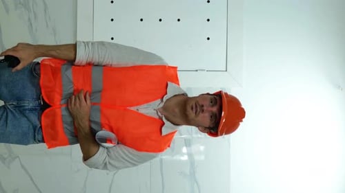 Male Builder in Waistcoat and Helmet Walking in a Building and Holding a Walkietalkie and Drawing