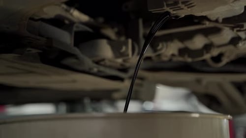 Auto Mechanic Drains Used Motor Oil From Car During Routine Service in Garage Vehicle Maintenance